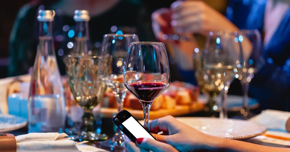 Close-up of a dinner table with wine glasses and smartphones in use, capturing modern social dining.