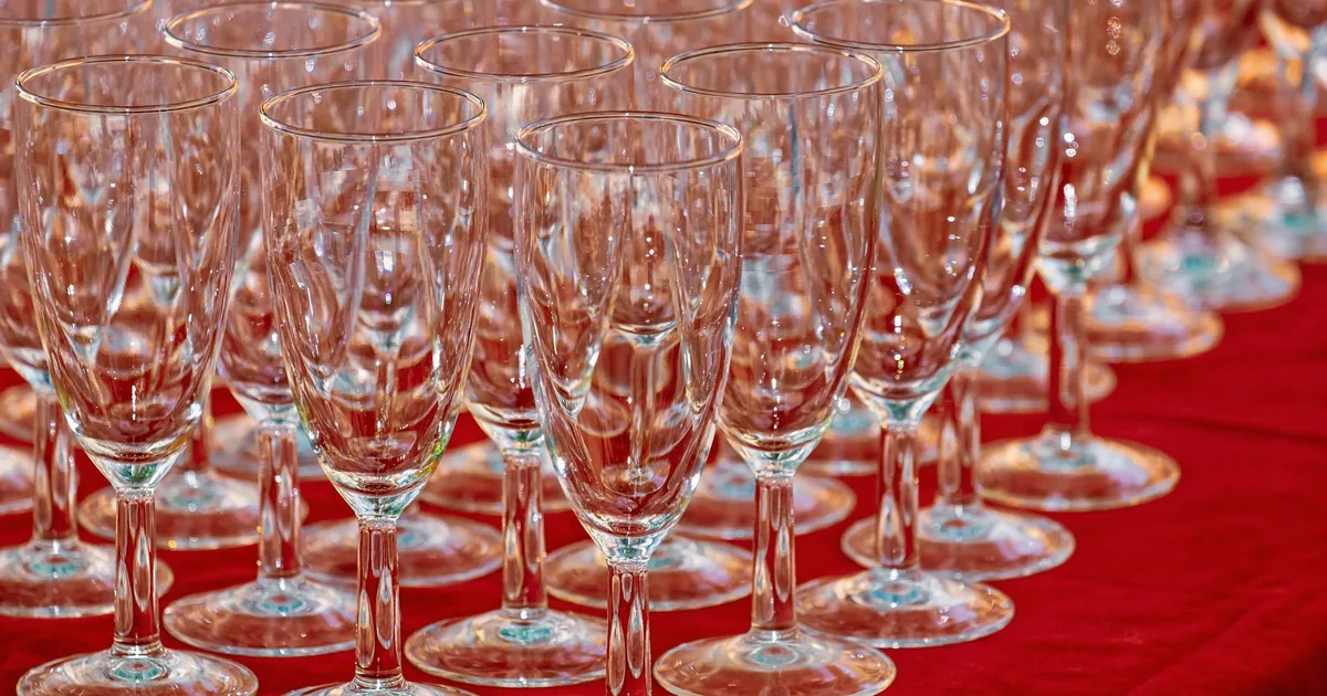 Rows of empty crystal glasses on a vibrant red tablecloth, ready for an event.