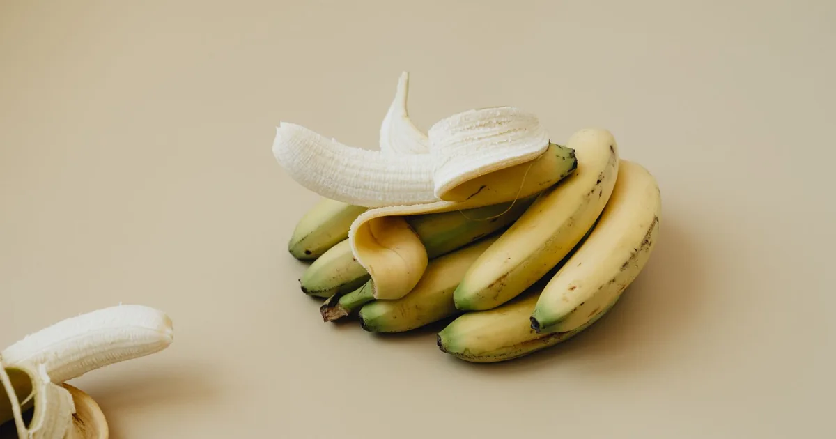 A bunch of ripe bananas with one peeled, displayed on a neutral backdrop. Ideal for food visuals.