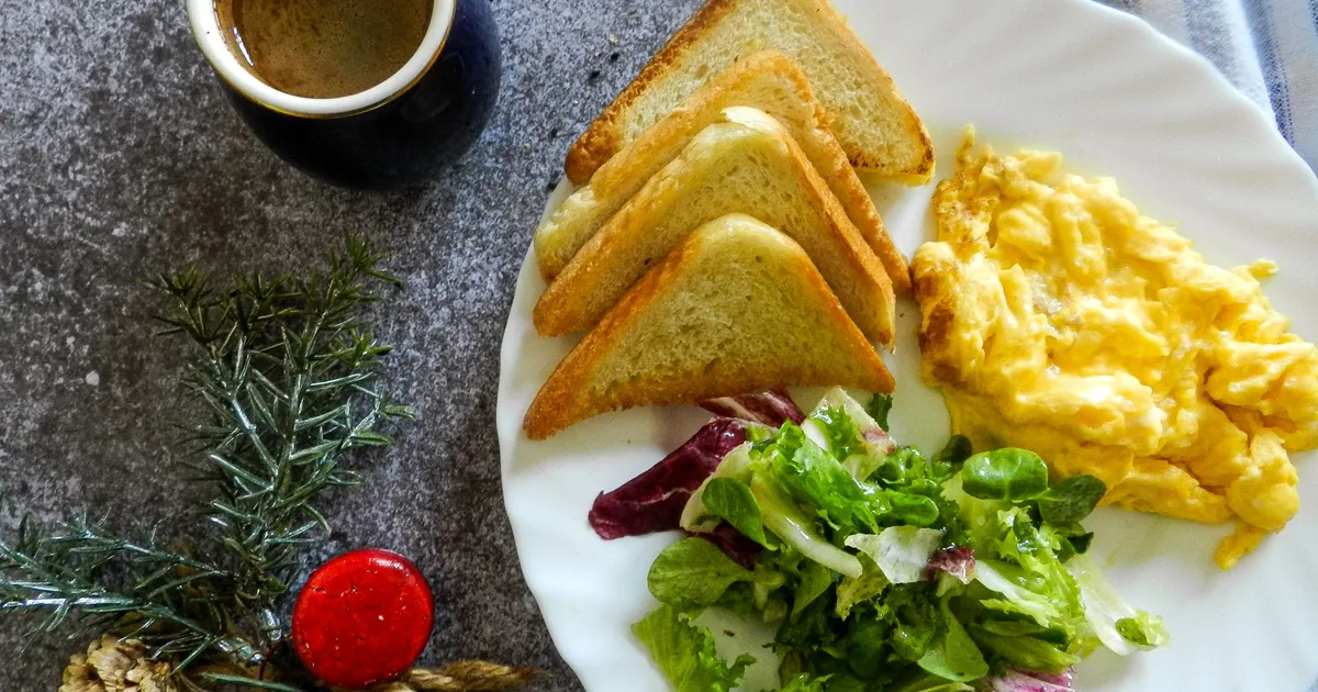 A breakfast plate with scrambled eggs, toast, salad, and coffee on a marble surface.