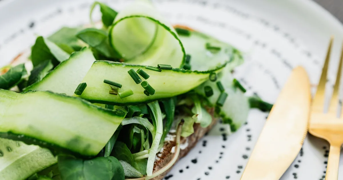 Fresh cucumber and chive sandwich on a plate with gold cutlery. Perfect for a healthy meal.