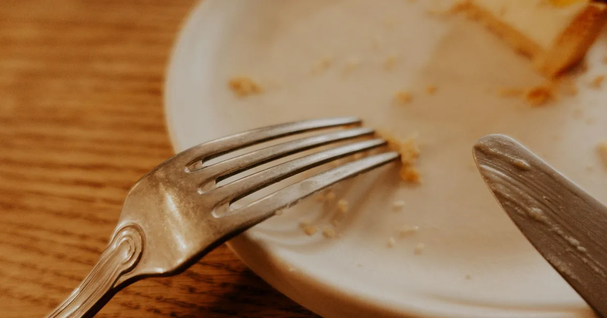 A close-up shot of a fork and knife on a plate with food remnants on a wooden table.