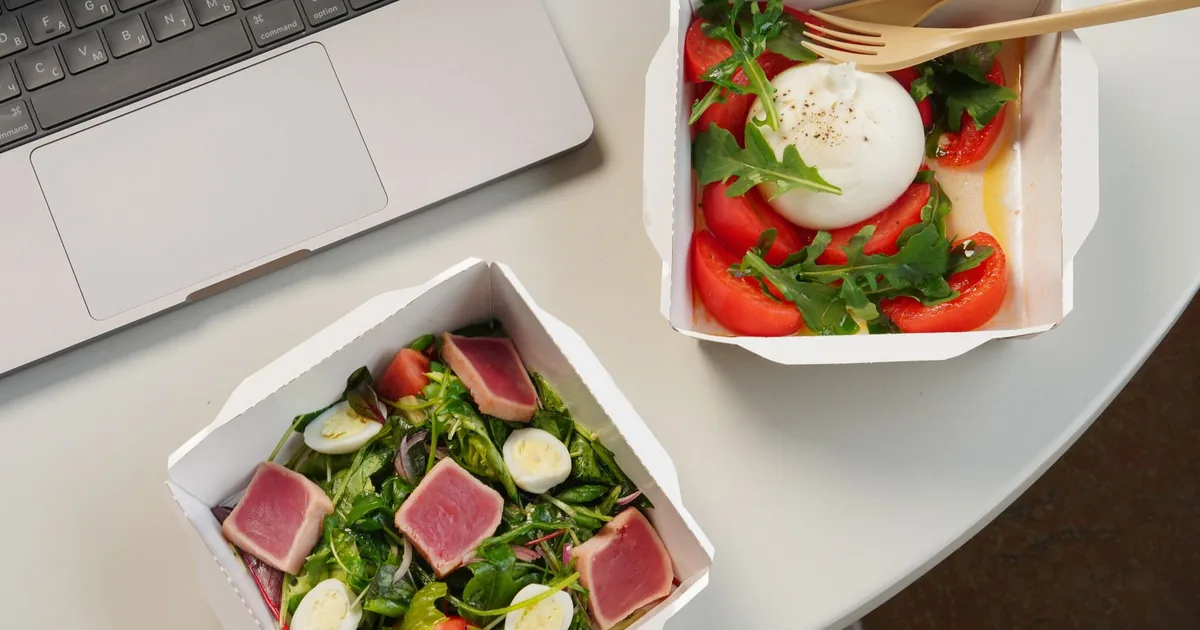 Top view of a desk setup with two fresh salads and a laptop, ideal for a healthy office lunch.