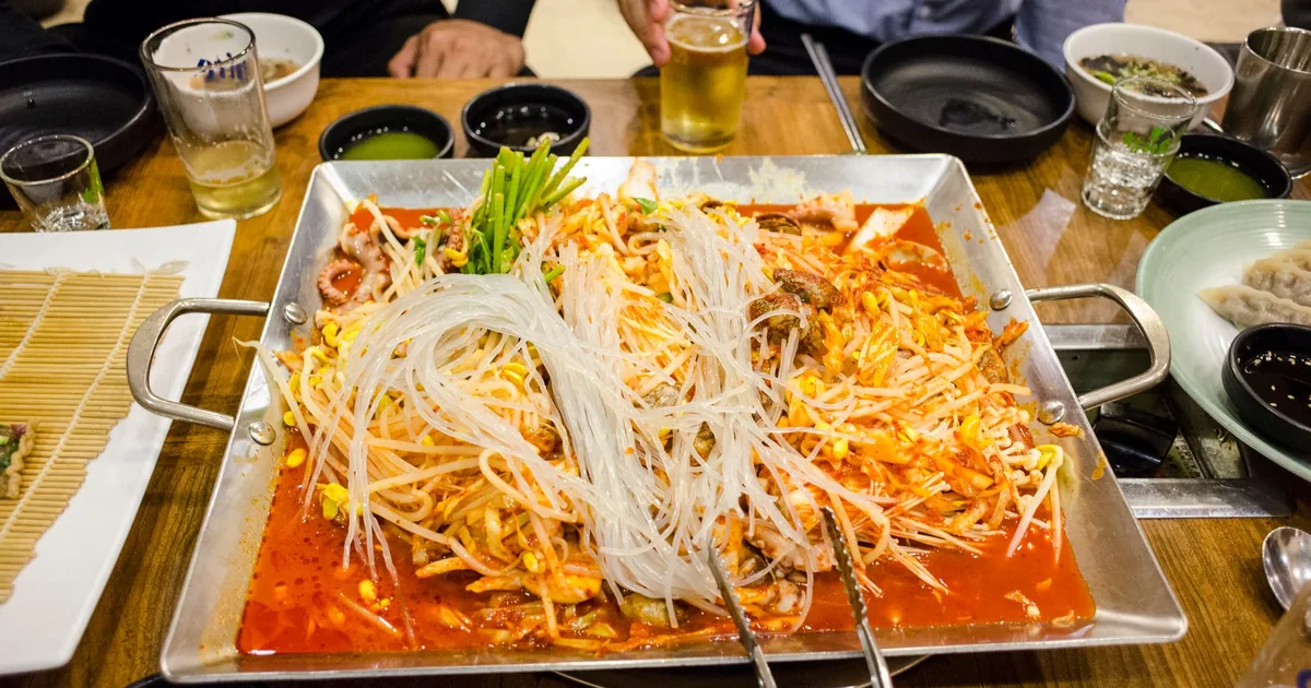 A vibrant tabletop spread featuring spicy Korean hot pot with rice noodles and various side dishes.