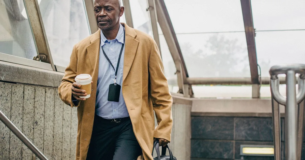 Pensive middle aged ethnic male office worker with takeaway coffee walking on staircase while looking down in building