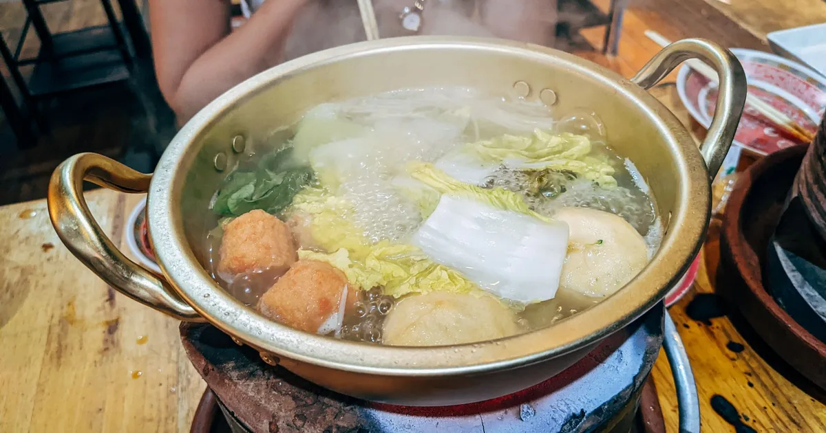 Steaming hot pot filled with fresh vegetables and meatballs, prepared on a stove.