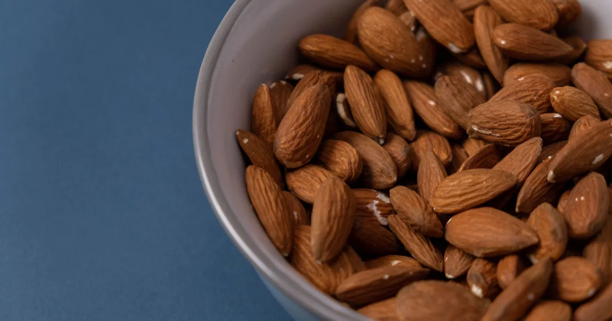 A bowl of fresh almonds on a blue background for healthy snack inspiration.