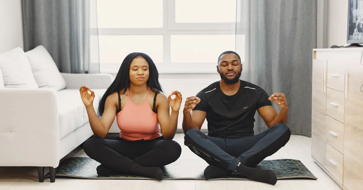 A couple meditating on yoga mats in a bright modern living room. Serenity and relaxation.