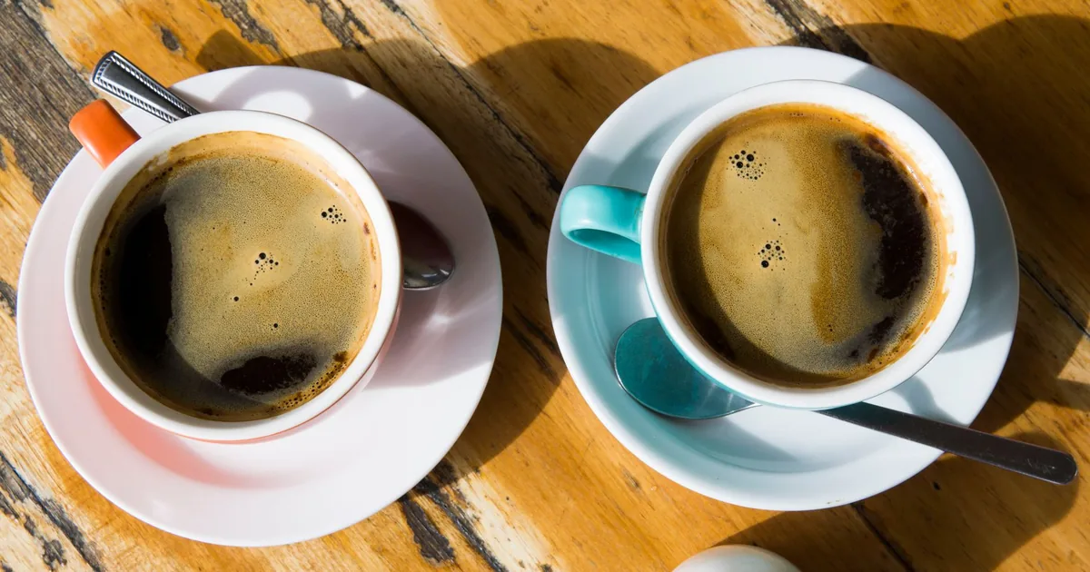 Top view of two black coffee cups on a sunny wooden table, Melbourne cafe vibe.