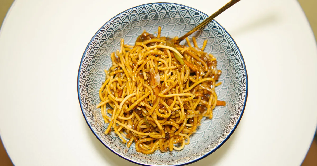 Appetizing Chinese noodles served in a decorative bowl with chopsticks on a table.