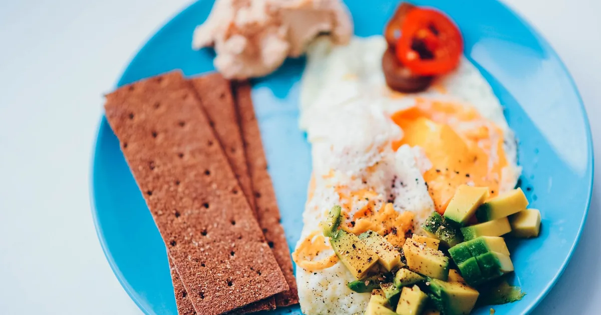 A vibrant breakfast plate featuring avocado, eggs, and crisp bread on a blue dish.