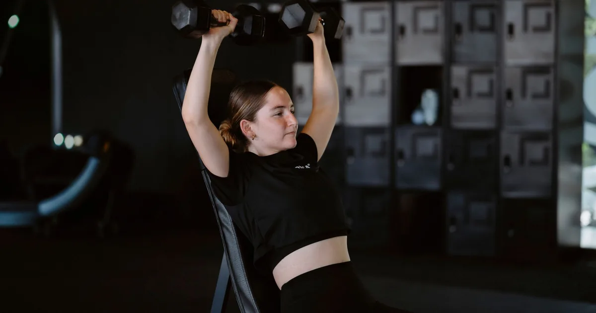 Young woman lifting dumbbells at gym showcasing strength training and fitness lifestyle.