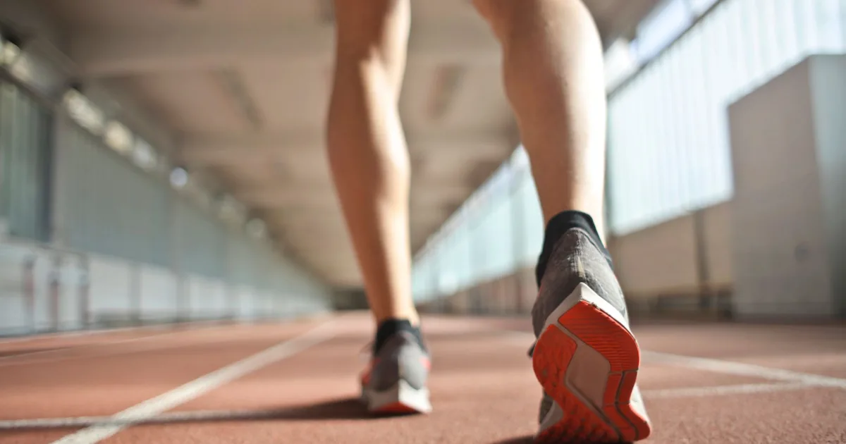 From below back view of crop athlete in sports shoes standing on running track while preparing for start during training