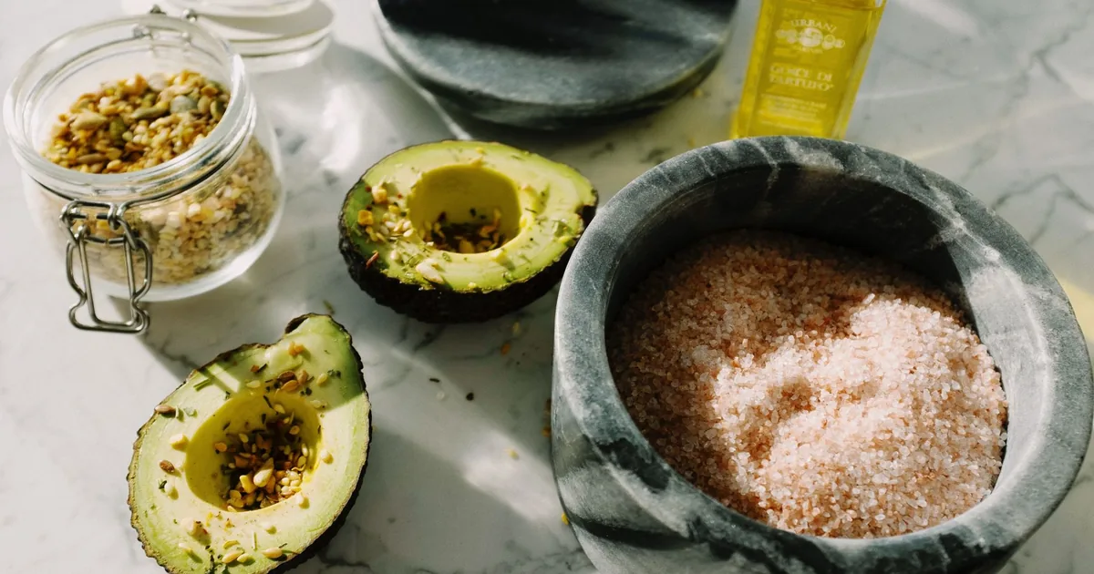 A close-up shot with avocado, pink salt, seeds, and olive oil combining for a healthy meal.