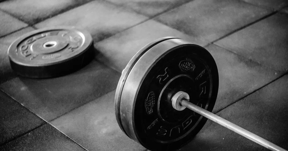 Grayscale image of heavy gym barbell and weights on rubber mat flooring.