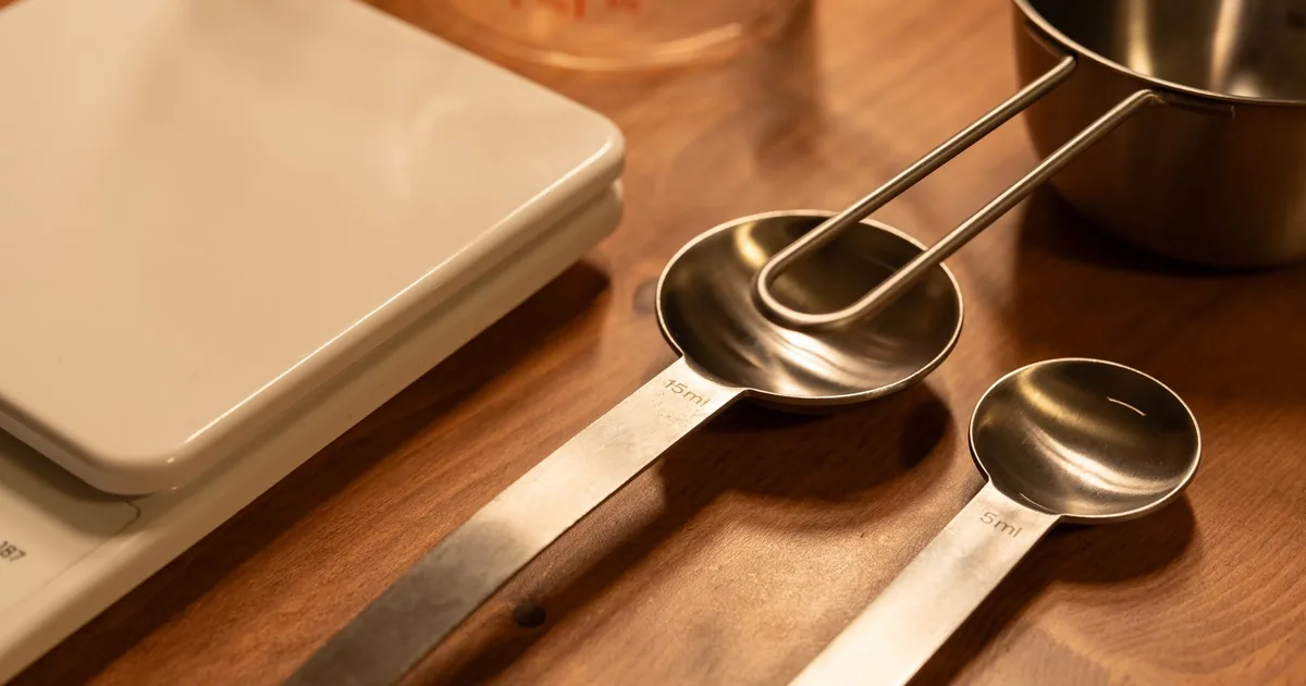 A close-up of kitchen utensils including a scale, measuring cups, and spoons on a wooden counter.