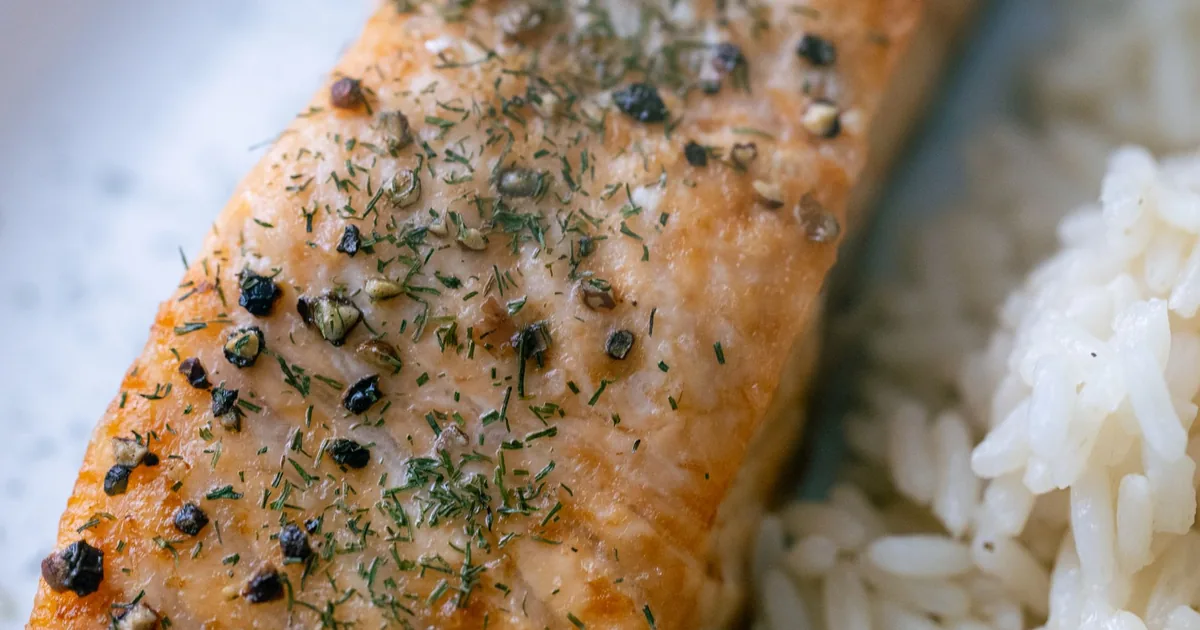 Close-up of a grilled salmon fillet with spices and rice on a white plate.