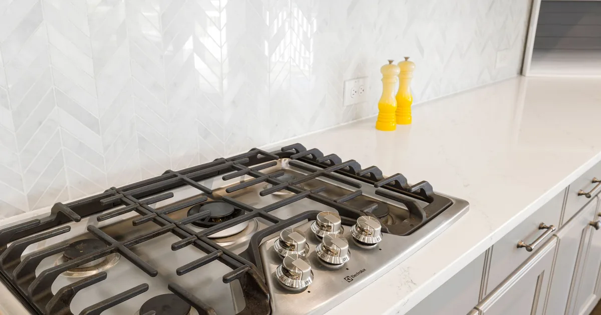 Sleek kitchen countertop featuring a gas stove and white tiled backsplash, with yellow salt and pepper shakers.
