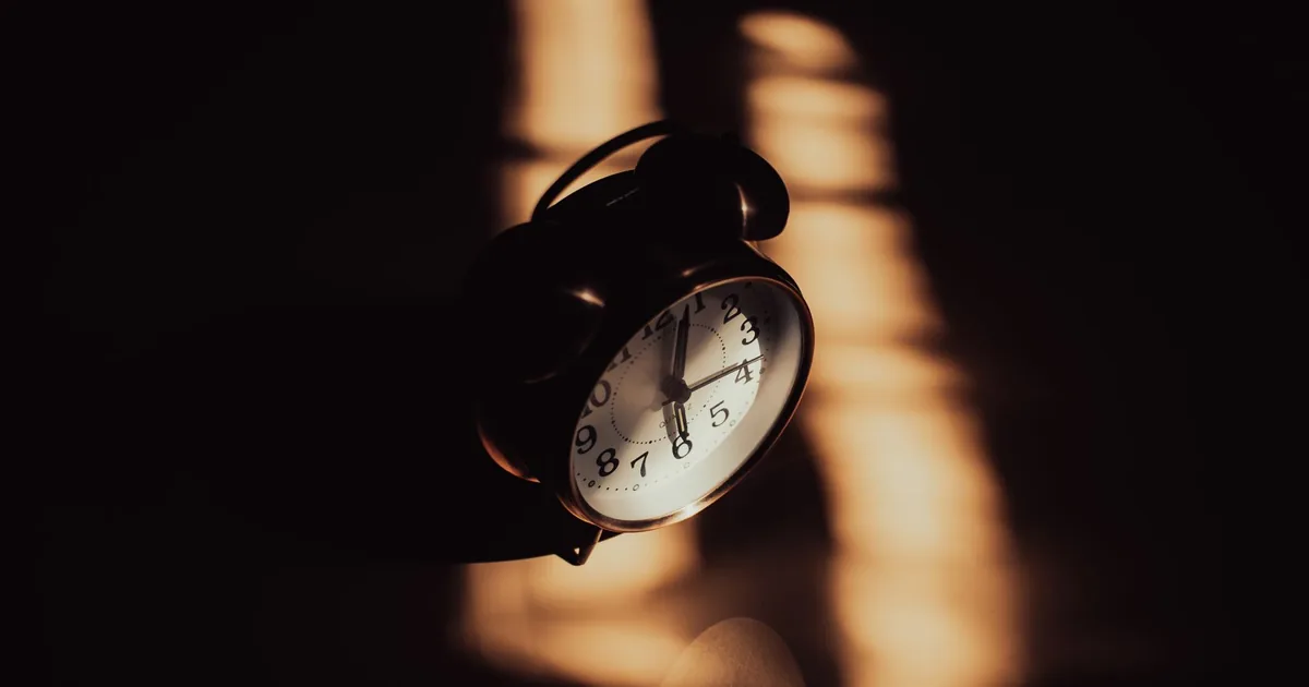 A retro analog alarm clock in moody shadows and warm lighting.