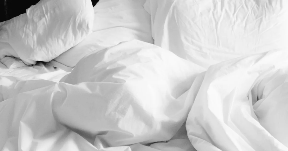 A cozy, rumpled white bed with soft sheets and pillows in a modern bedroom setting.