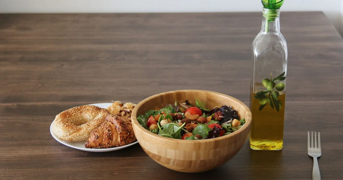 A vibrant vegetable salad with bagel and croissant, olive oil on a wooden table.