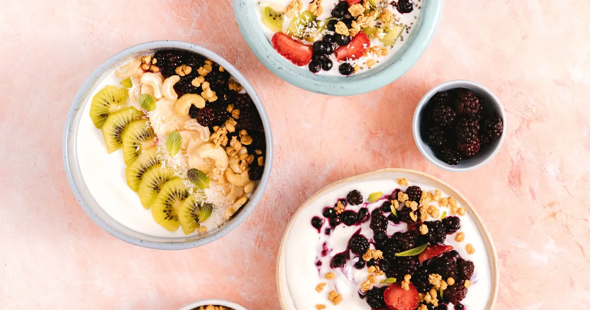 Top view of yogurt bowls topped with fresh fruits and nuts on a textured background.
