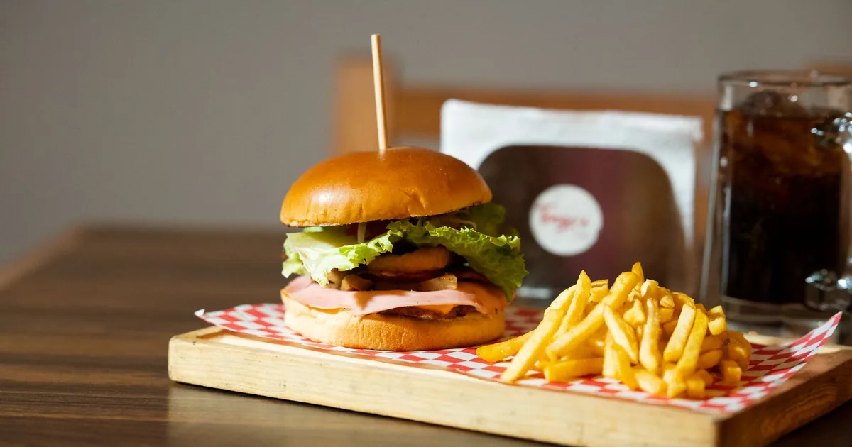 Delicious gourmet burger with fries and drink on a wooden tray. Perfect for fast food lovers.