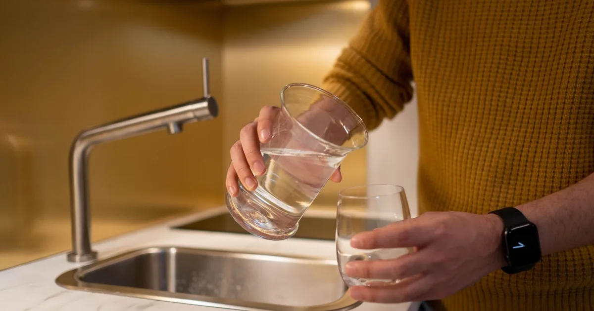 Person pouring water from a pitcher into a glass in a contemporary kitchen setting.