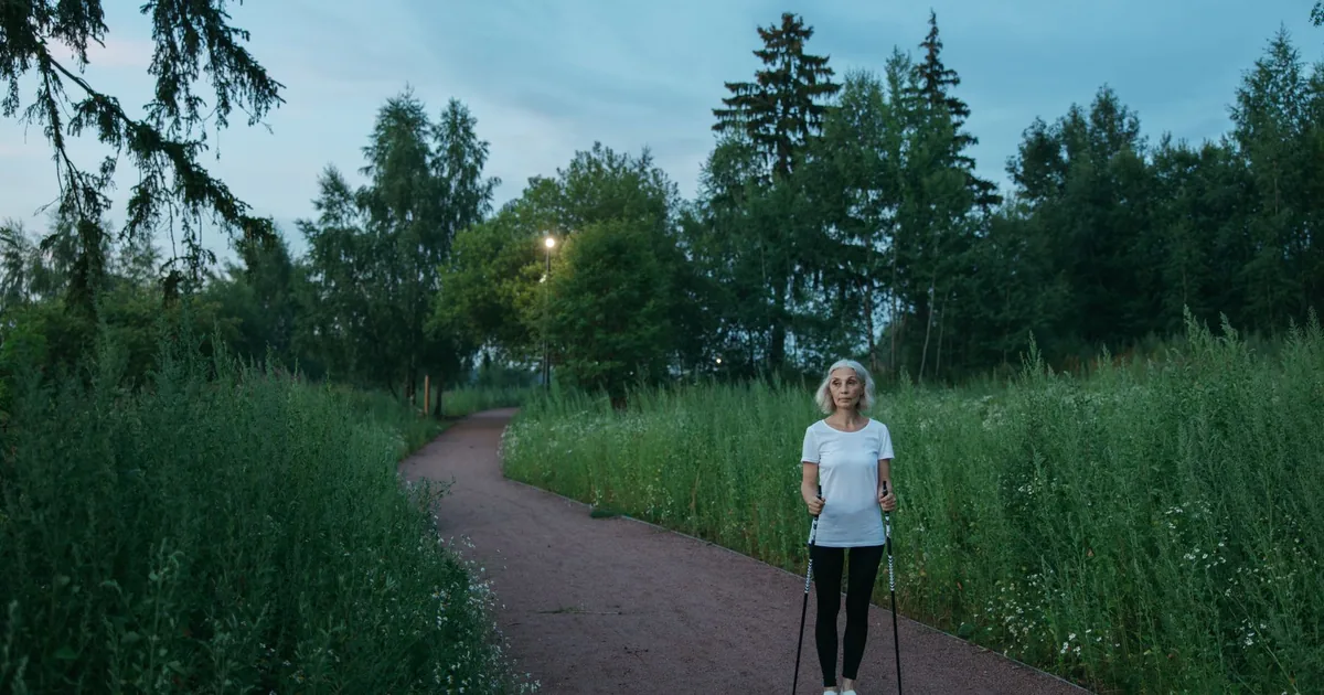 Senior woman exercising with Nordic walking poles in a peaceful green park during daytime.