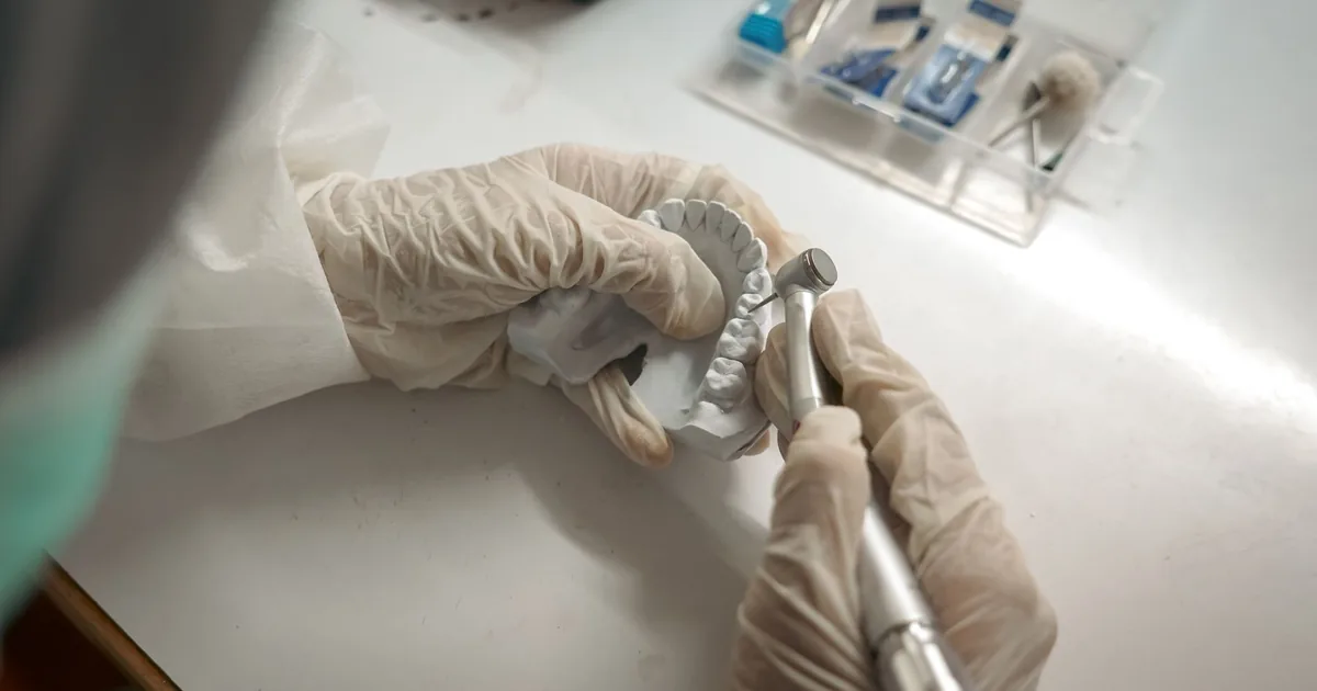 Dentist crafting dental prosthetics with precision tools and gloves.
