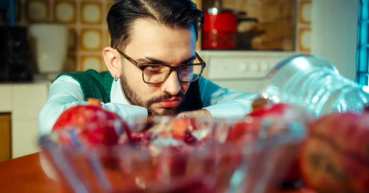 Man in glasses looks thoughtfully at fruit on a kitchen table.